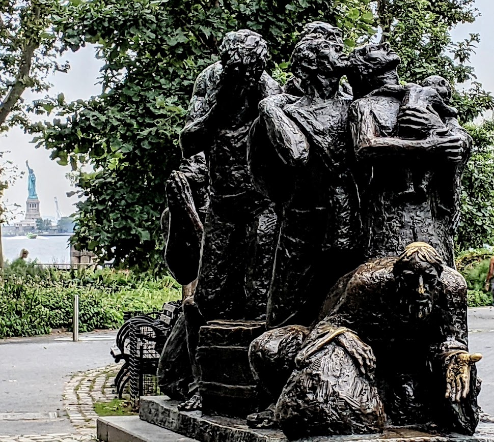 Immigrants statue at Battery Park, NYC with Statue of Liberty